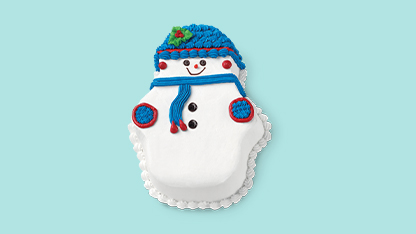 Cute cake shaped like a snowman. It has a face and a Santa hat, adorned with red and blue details. The background is light blue, providing a stark contrast to the snowman-cake.