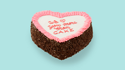 A chocolate cake with a heart shaped decoration and writing that reads, "With love from your friend, Sharon." The cake is decorated in pink and brown colors.